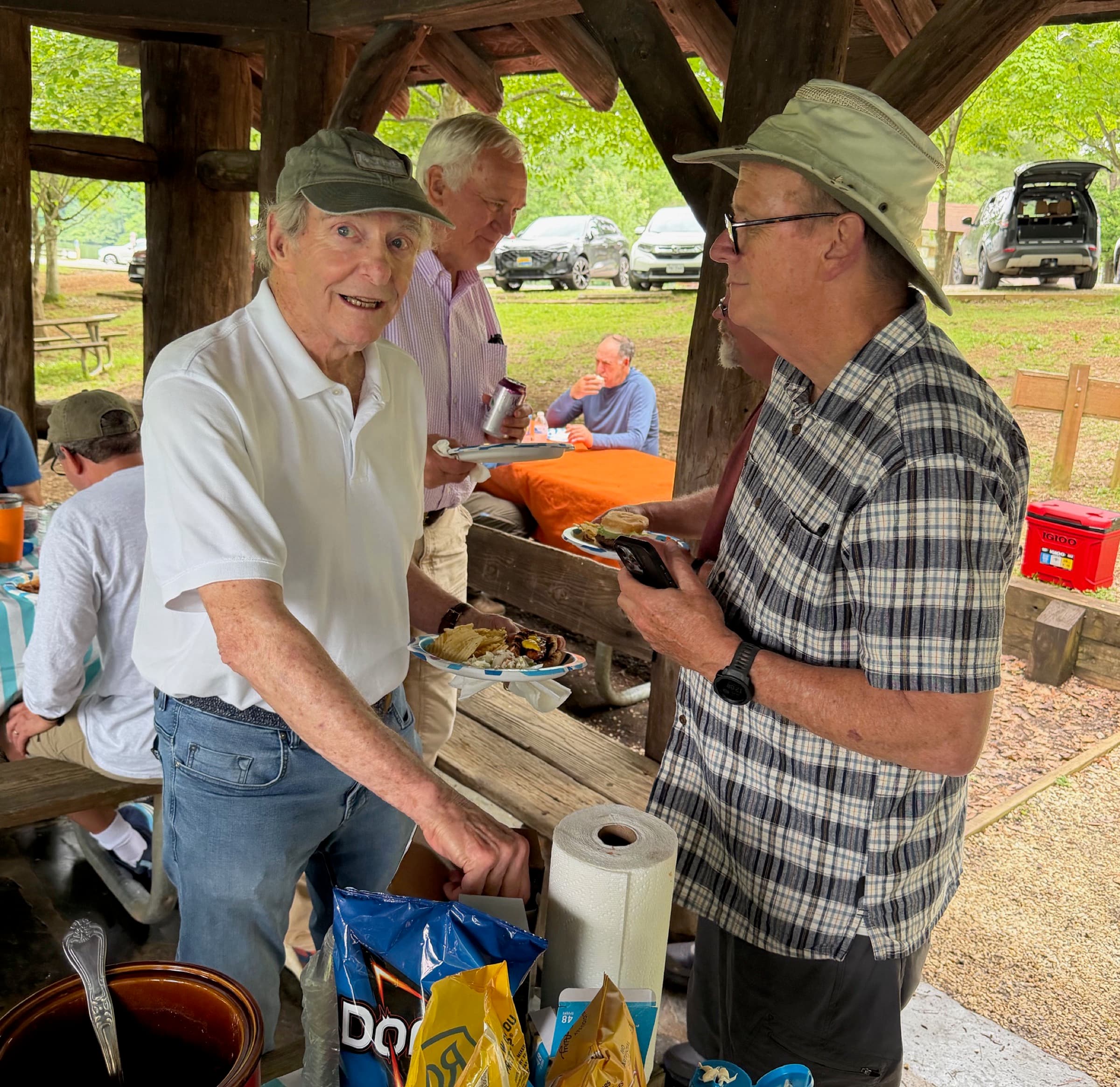 Two hikers in conversation at the cookout, plates in hand, under the park shelter.